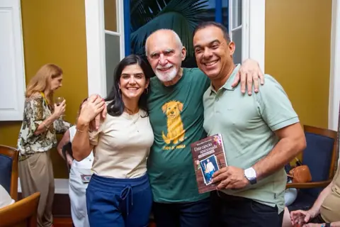 Benedito Furtado posa com convidados durante encontro literário, segurando um de seus livros.